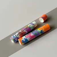 View: Two cardboard lip balm tubes with floral artwork lying at an angle on a grey background