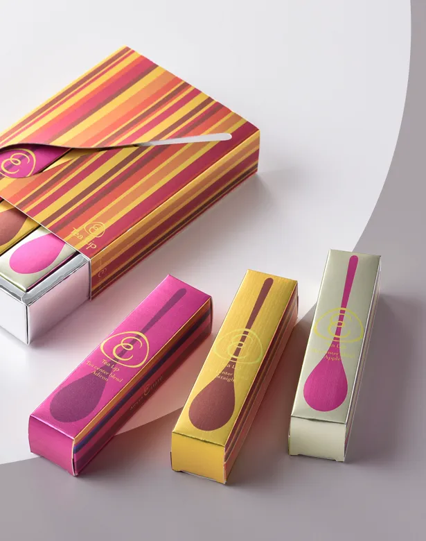 Striped lip care gift box open beside three matching slim cartons in pink, yellow and cream