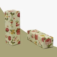 View: Two floral printed lipstick boxes, one standing and one lying flat on an olive background