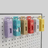 View: Six coloured hang tab lip balm boxes hanging in a row from hooks on a white pegboard display