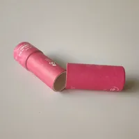 View: Two magenta printed paper lip balm tubes lying on a grey surface, one with its cap removed
