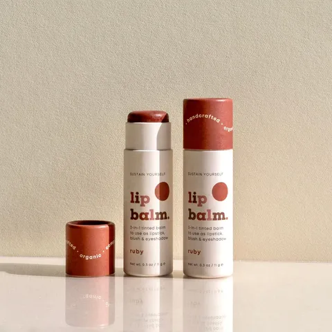 Two printed kraft paper lip balm tubes in terracotta and cream standing upright with their caps removed