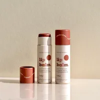 View: Two printed kraft paper lip balm tubes in terracotta and cream standing upright with their caps removed