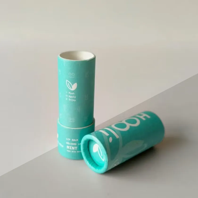 Two teal printed paper lip balm tubes lying at an angle, one showing the open push-up chamber